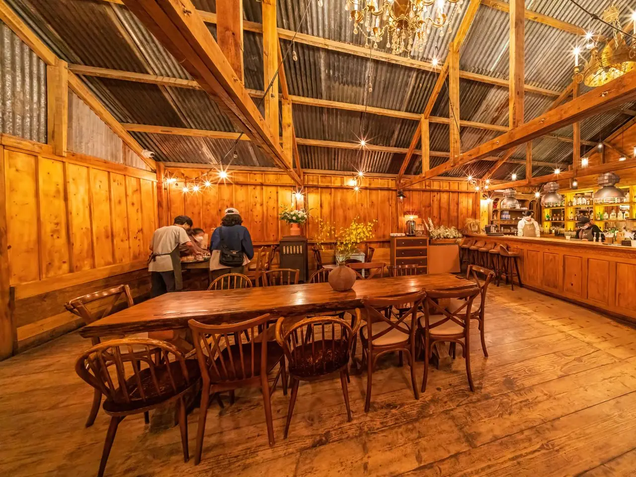 The barn café: a long wooden table and chairs under timber beams and strings of lights