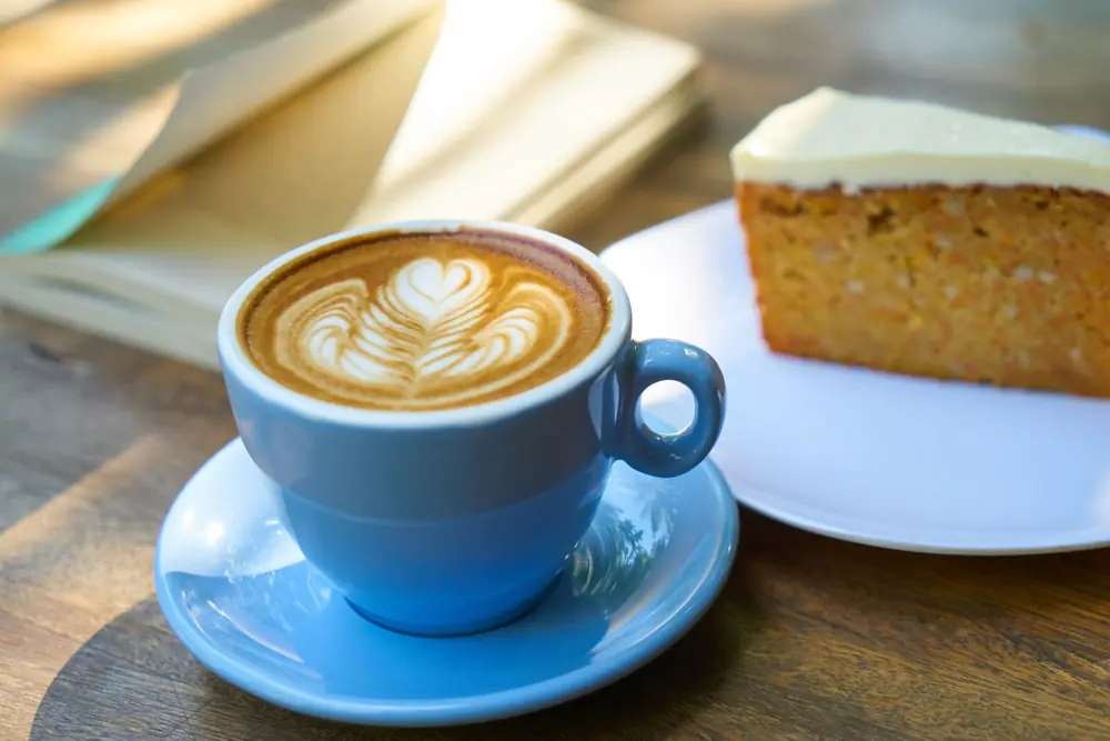 A cappuccino in a blue cup beside a slice of carrot cake