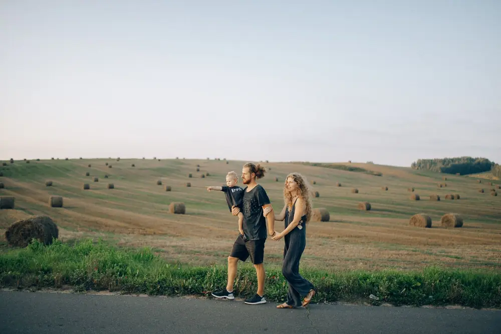 A couple and a small child walking beside a field of round hay bales
