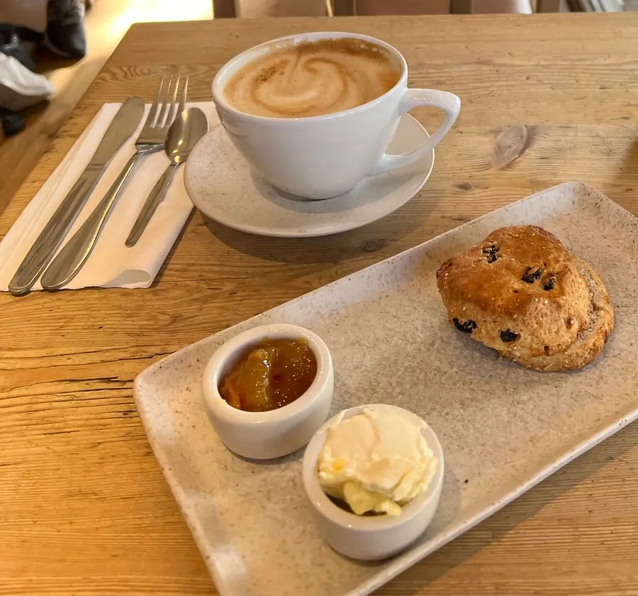 A fruit scone with jam and cream beside a cup of coffee