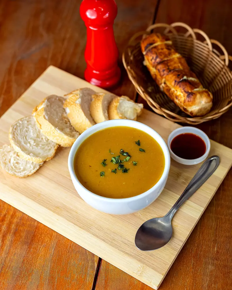 A bowl of vegetable soup on a wooden board with sliced bread