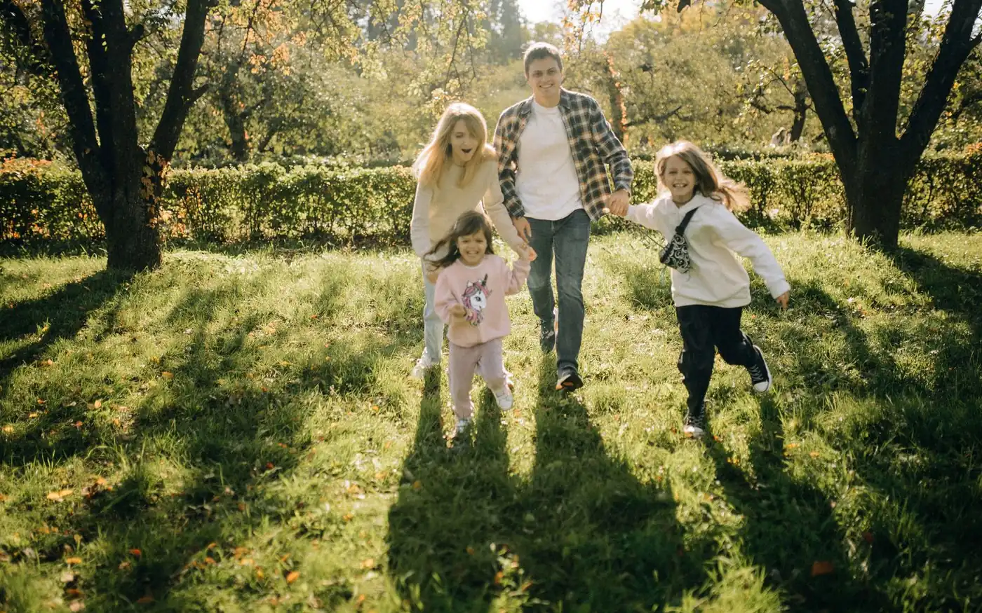 A family of four running hand in hand across sunlit grass
