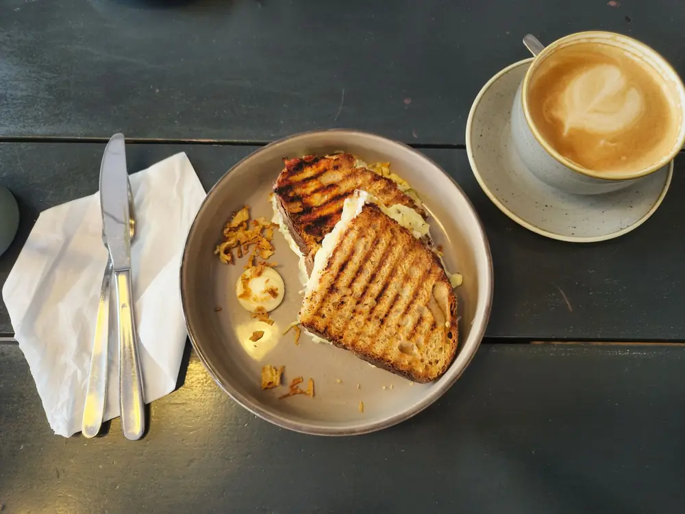 A toasted cheese sandwich on a plate with a cup of coffee