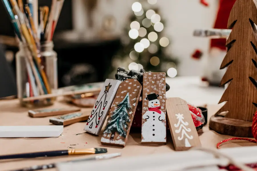Hand-painted wooden Christmas decorations on a craft table with brushes